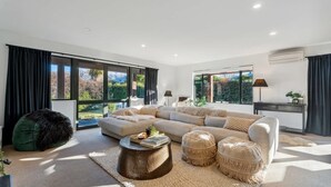 A modern living room with a large sectional sofa, a green bean bag chair, a round coffee table, and a view of a mountainous landscape through large windows. - Scenic Wanaka House with Mountain Views (Wanaka)