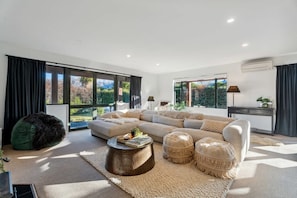 A modern living room with a large sectional sofa, a green bean bag chair, a round coffee table, and a view of a mountainous landscape through large windows.