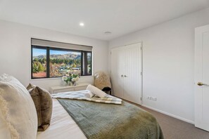 Un dormitorio con un ventanal grande, una cama, una mesita de noche con un jarrón de flores y un armario.