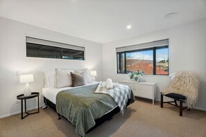 Un dormitorio con cama, dos mesitas de noche, una lámpara auxiliar y una ventana con vistas, además de una silla.