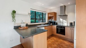 A modern kitchen with a window, wooden cabinets, a black countertop, and a built-in oven. - Scenic Wanaka House with Mountain Views (Wanaka)
