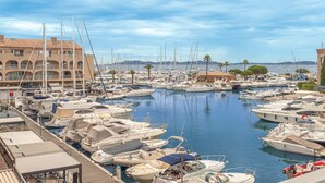 Un puerto deportivo con numerosas embarcaciones amarradas, un edificio con balcones y un cielo despejado.