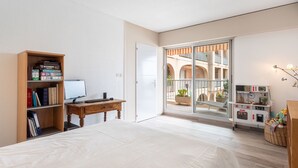 Un dormitorio con una cama, un escritorio con ordenador, una estantería y vistas a un patio exterior.