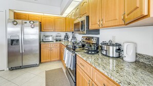 A modern kitchen with wooden cabinets, stainless steel appliances, granite countertops, and a ceiling fan. - Port Charlotte Home ~ 3 Mi to Beach & Harbor! (Port Charlotte)