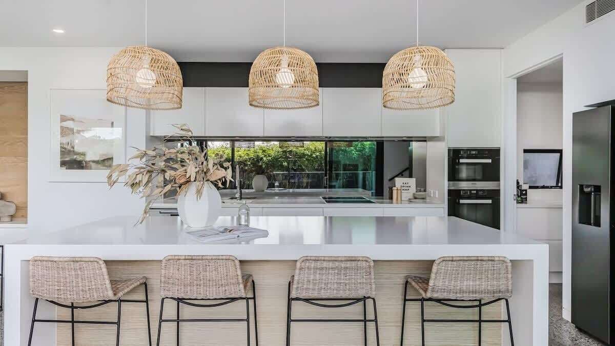 A modern kitchen with a central island, three wicker pendant lights, and a view of the outdoors.