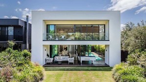 A modern two-story house with a glass balcony, a pool, and a well-maintained garden. - Oceans Echo (Casuarina)