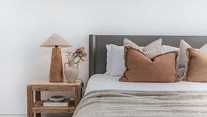 A bedroom with a bed, pillows, a bedside table with a lamp, a vase, and a book. - Oceans Echo (Casuarina)