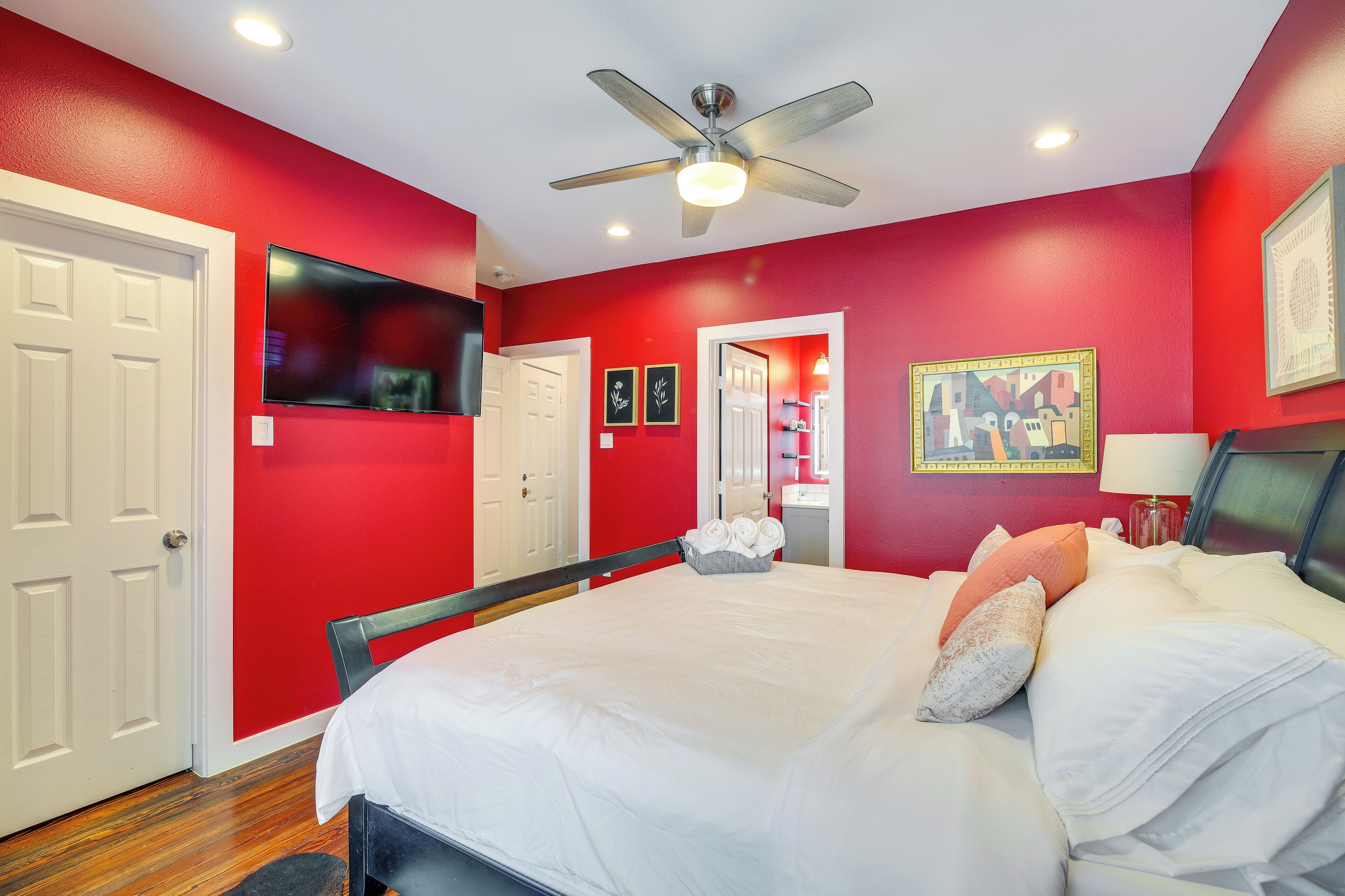 Une chambre à coucher avec un lit, un ventilateur de plafond, une télévision et un mur rouge.