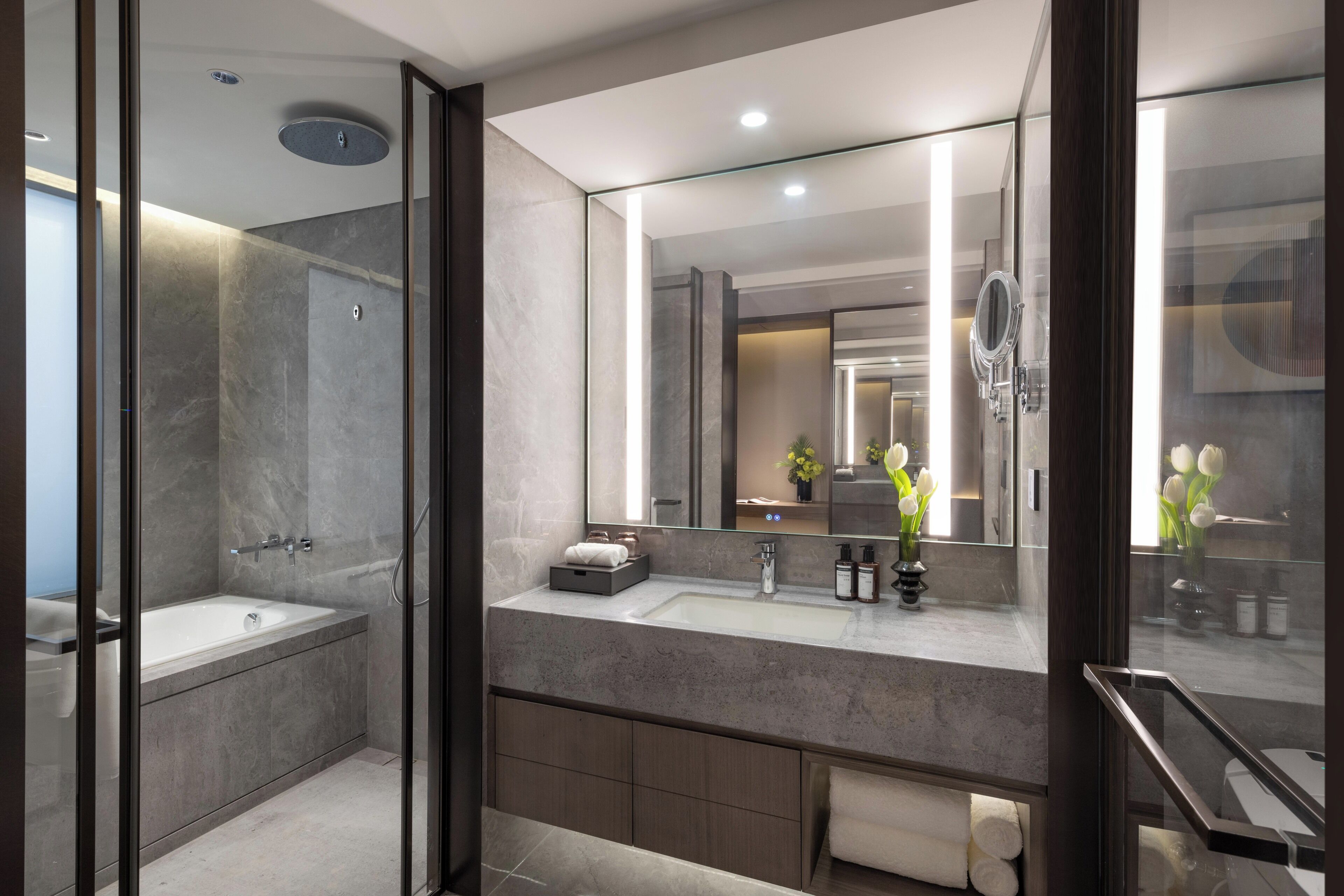 A modern bathroom with a glass-enclosed shower, a large mirror, and a vanity with a sink and countertop.