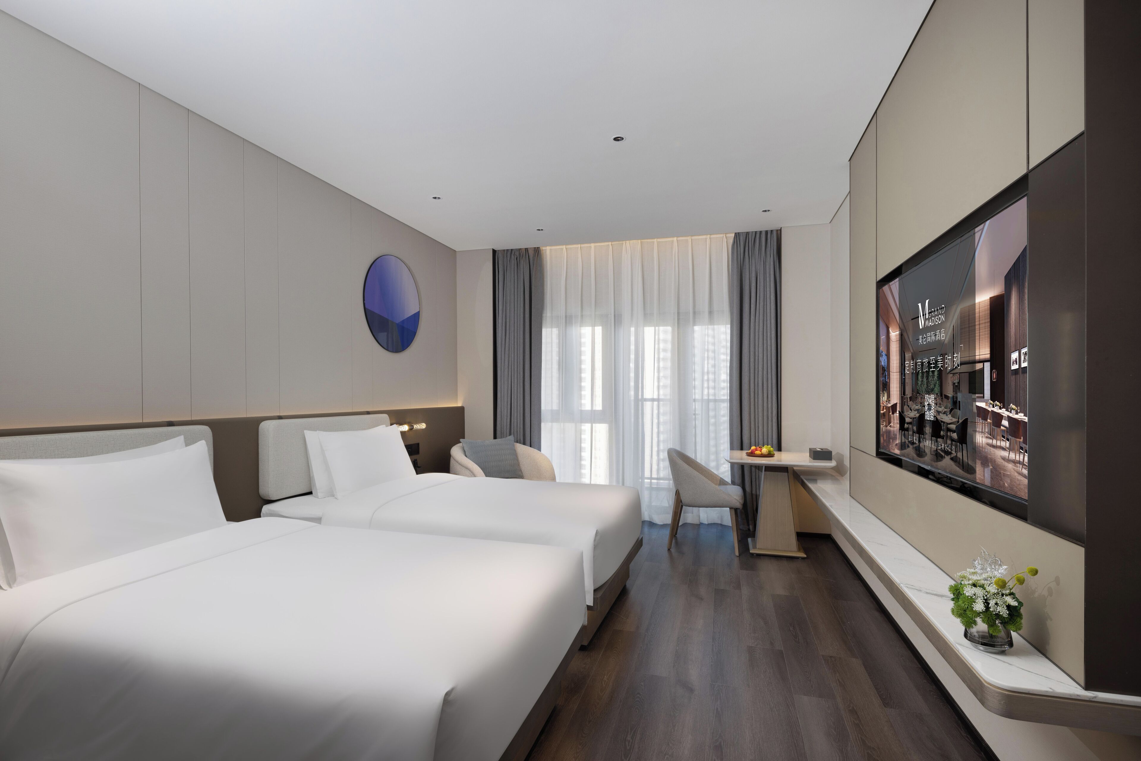 A hotel room with two beds, a desk, a TV, and a large window with curtains.