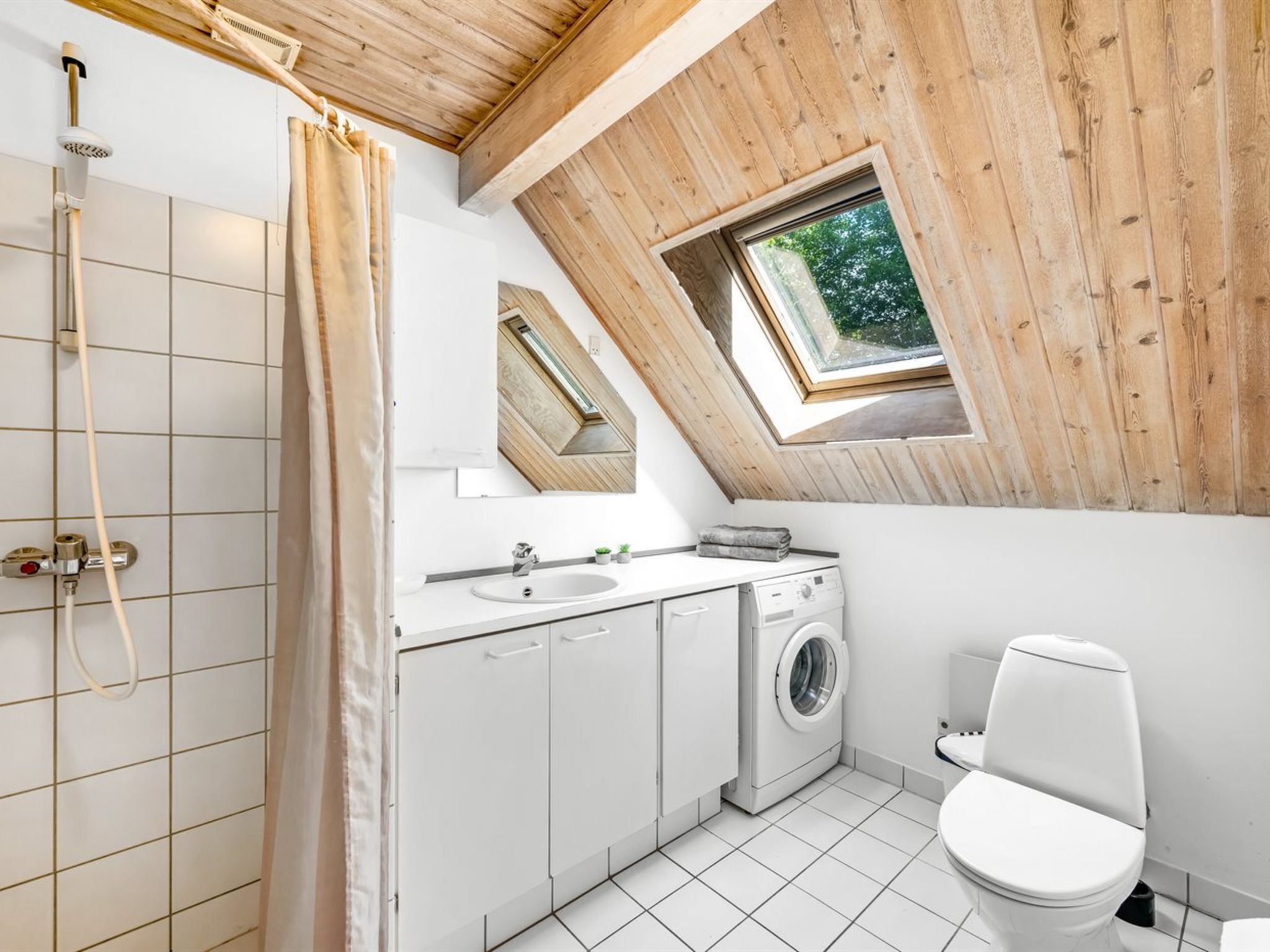 A bathroom with a skylight, a shower, a sink, a washing machine, and a toilet.