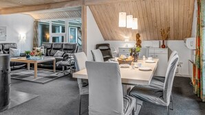 Un espace de vie et de salle à manger moderne, à aire ouverte, doté d’un plafond en pente, de poutres en bois et d’une grande fenêtre qui laisse entrer la lumière naturelle.