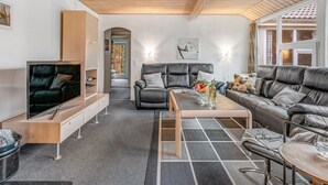 Un salon moderne avec un plafond en bois, un canapé en cuir noir, un canapé gris, une table basse en bois et un téléviseur posé sur un meuble en bois.