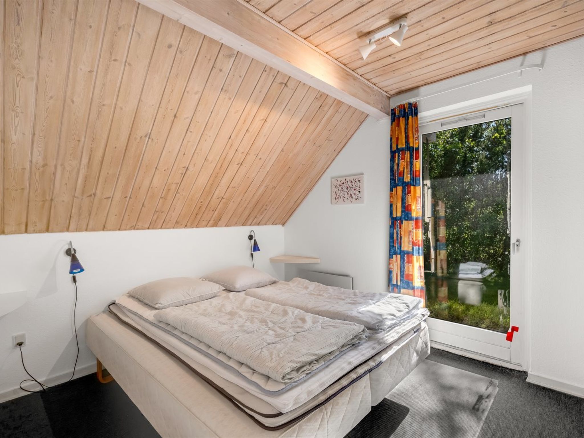 Una camera da letto con soffitto spiovente, un letto, una scrivania e vista panoramica attraverso una porta in vetro.