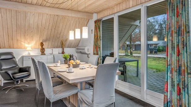 Une cuisine moderne avec un plafond en bois, une table à manger avec des chaises et une vue sur l’extérieur grâce à de grandes fenêtres.