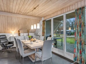 Une cuisine moderne avec un plafond en bois, une table à manger avec des chaises et une vue sur l’extérieur grâce à de grandes fenêtres.