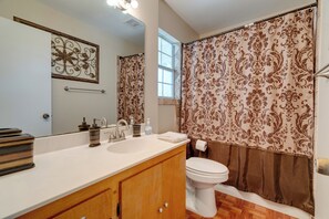 Un bagno con uno specchio grande, un lavabo con dispenser di sapone, un water e una tenda da doccia con motivo floreale.