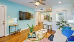 A modern living room with a ceiling fan, a glass coffee table, a sofa, and a kitchen area in the background. - Central Houston Apartment w/ Furnished Patio! (Houston)