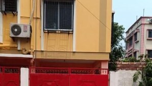 A yellow building with a red gate and a concrete driveway. - Regencyy Guest House (Kolkata)
