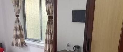Habitación de hotel con dos camas, un armario, un escritorio, una silla, una ventana con cortinas y un televisor en la pared.