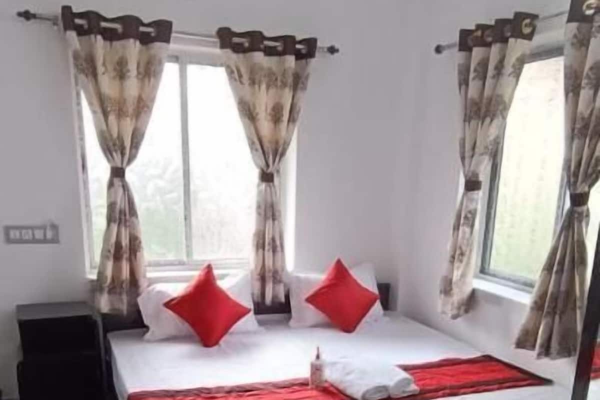 Une chambre à coucher avec un lit, deux fenêtres avec des rideaux, un ventilateur de plafond et une petite table.