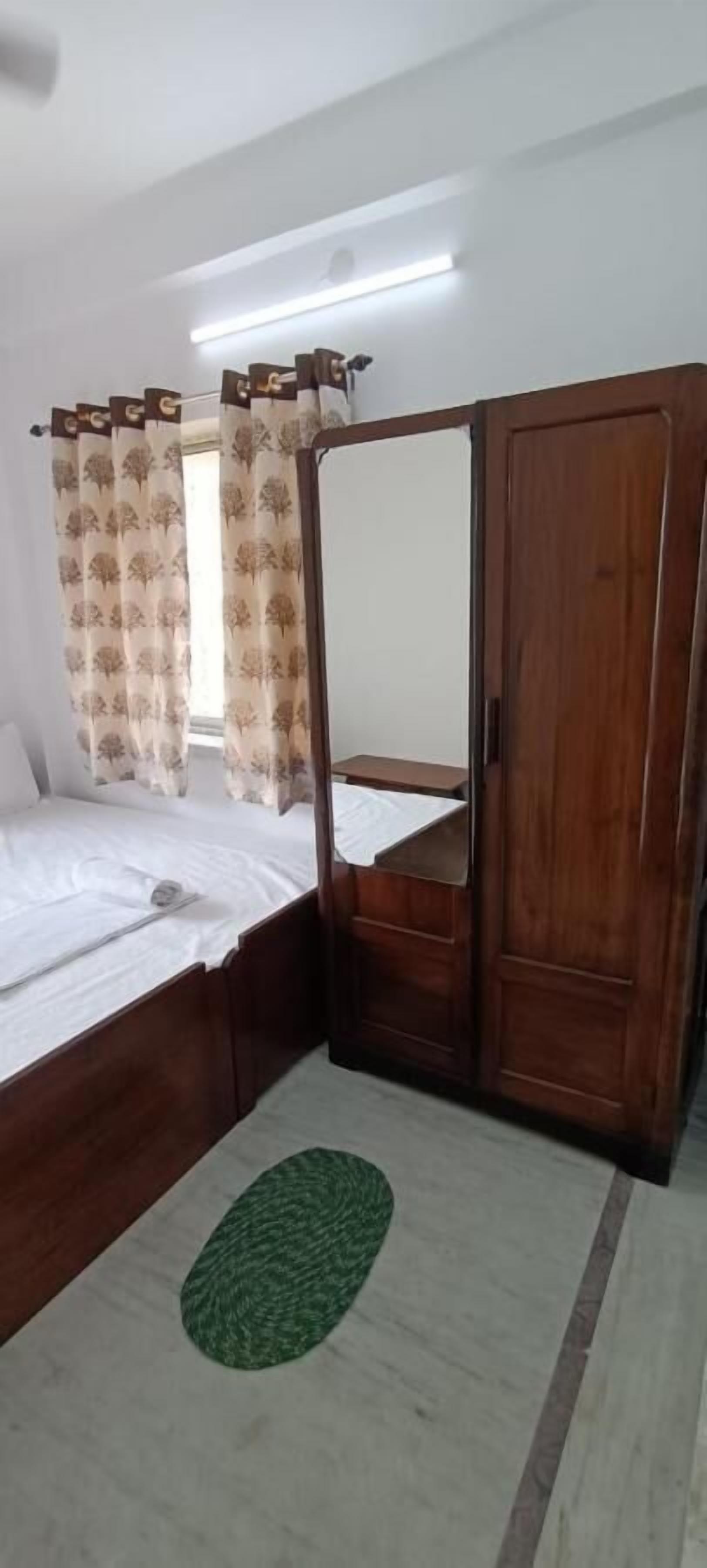A bedroom with a bed, a wardrobe, a mirror, and a green rug.