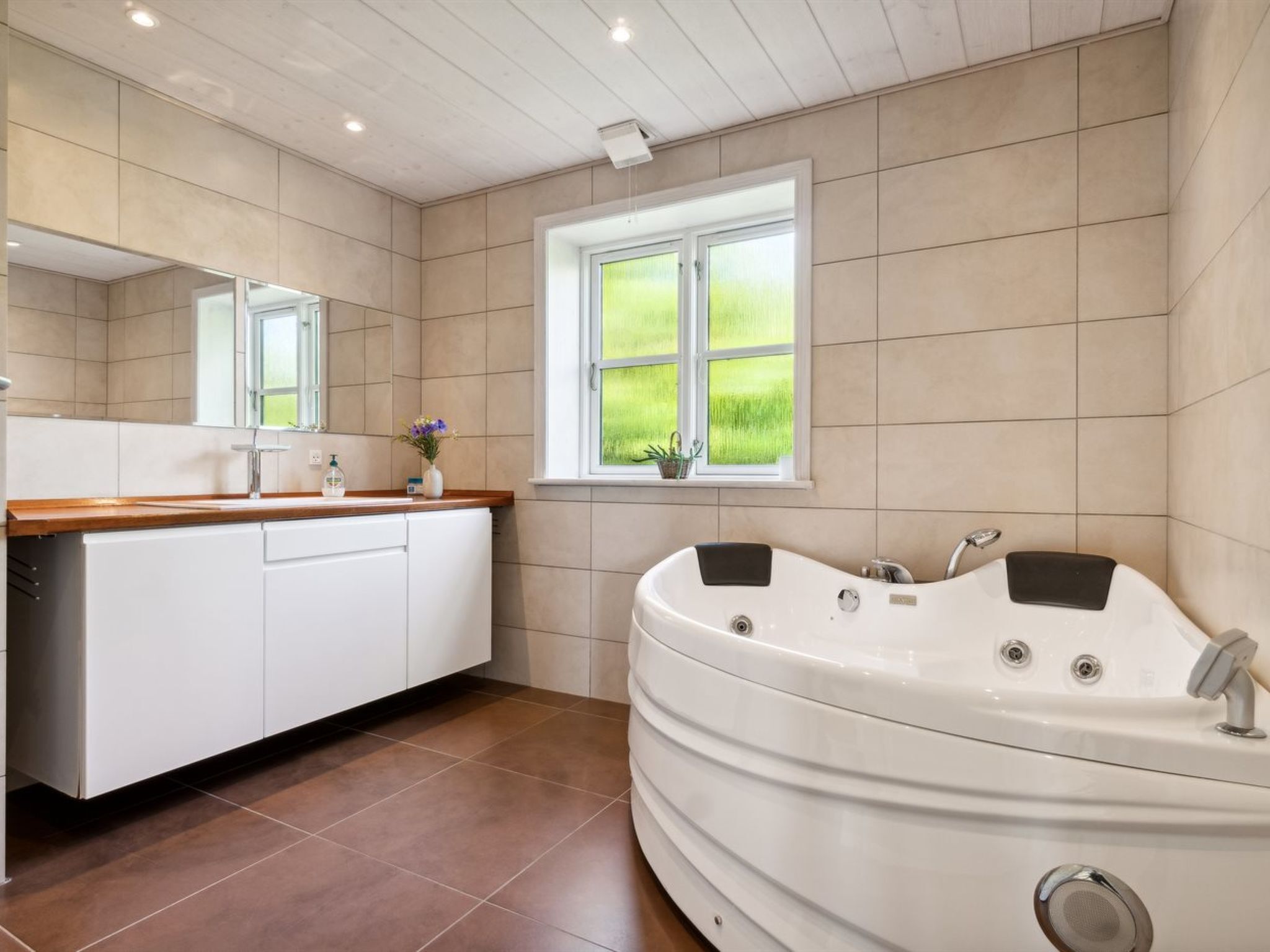 Een moderne badkamer met een vrijstaand bad, een wastafel met spiegel en een raam met uitzicht op groen.