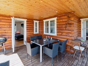 Une cabane en rondins dotée d’un coin repas avec une table et des chaises, d’un barbecue à l’extérieur et d’une chambre visible à travers une porte ouverte.
