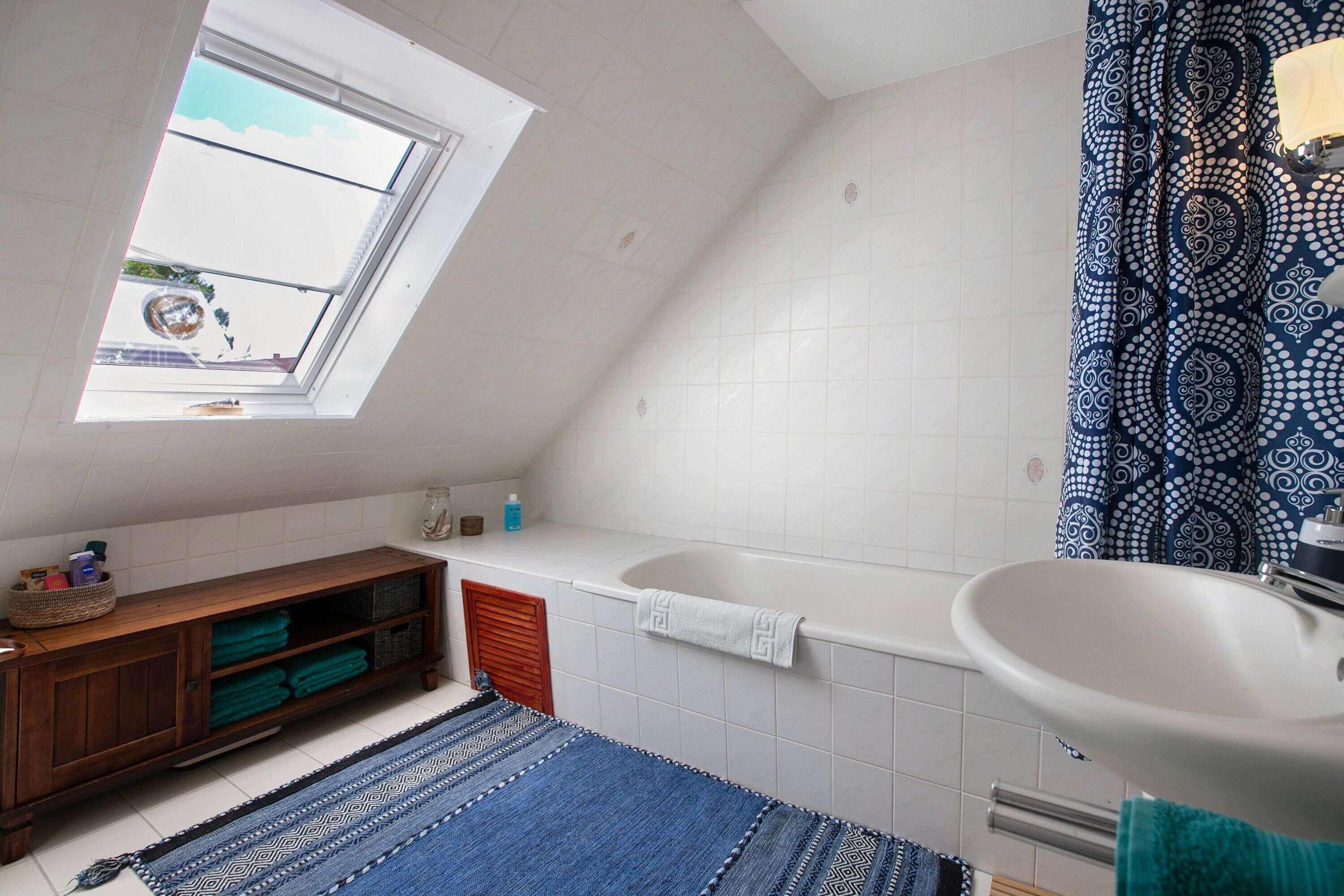 A bathroom with a skylight, a bathtub, a sink, a wooden cabinet, and a patterned shower curtain.