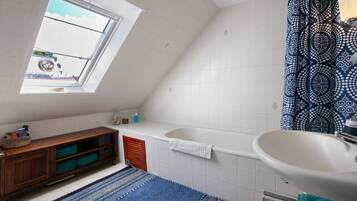 A bathroom with a skylight, a bathtub, a sink, a wooden cabinet, and a patterned shower curtain.