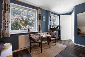 Una habitación con una mesa de comedor, dos sillas, un radiador y una ventana con cortinas.