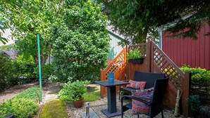 Une terrasse avec une table et des chaises, entourée de verdure et d’une clôture en bois.