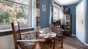 Une pièce avec une table à manger dressée pour deux personnes, une fenêtre avec des rideaux, un radiateur et un meuble avec des portes en verre.