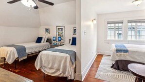 A hotel room with two single beds, a ceiling fan, a window with blinds, and a small table with a lamp.