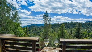 A wooden bench with two wine glasses on it, overlooking a forested mountain landscape.