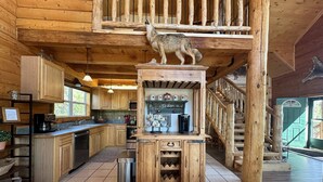 A rustic cabin interior with wooden floors, a kitchen with wooden cabinets, a dining area, and a staircase.