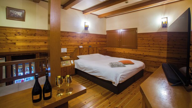 A wooden-paneled room with a bed, a desk, and a TV. There are two bottles and a glass on the desk. - Hotel St.River - Adult only (Toyama)