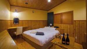 A wooden-paneled room with a bed, a desk, and two wine bottles on a table. - Hotel St.River - Adult only (Toyama)