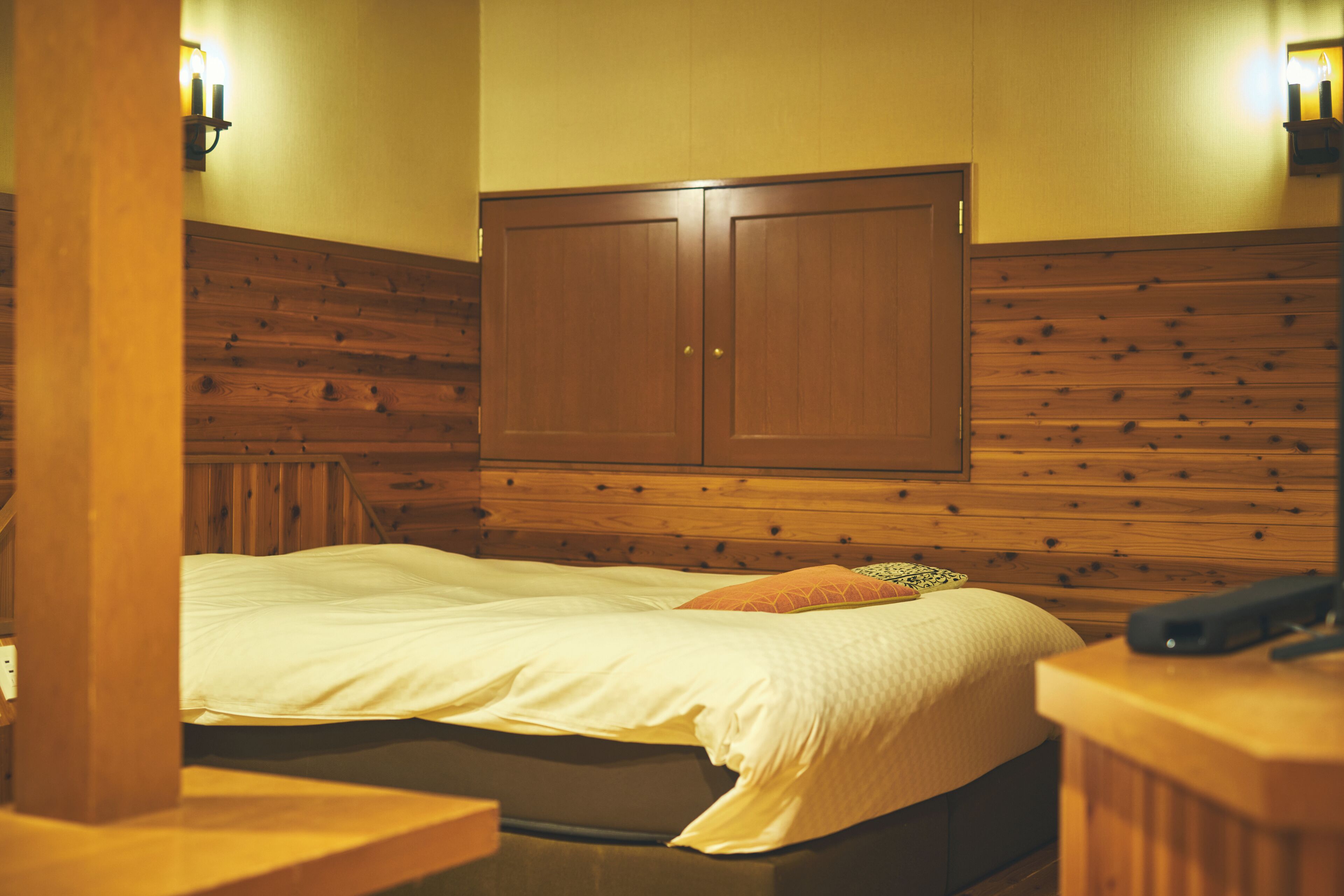 A room with a bed, wooden paneling on the walls, a wardrobe, and a nightstand with a lamp.