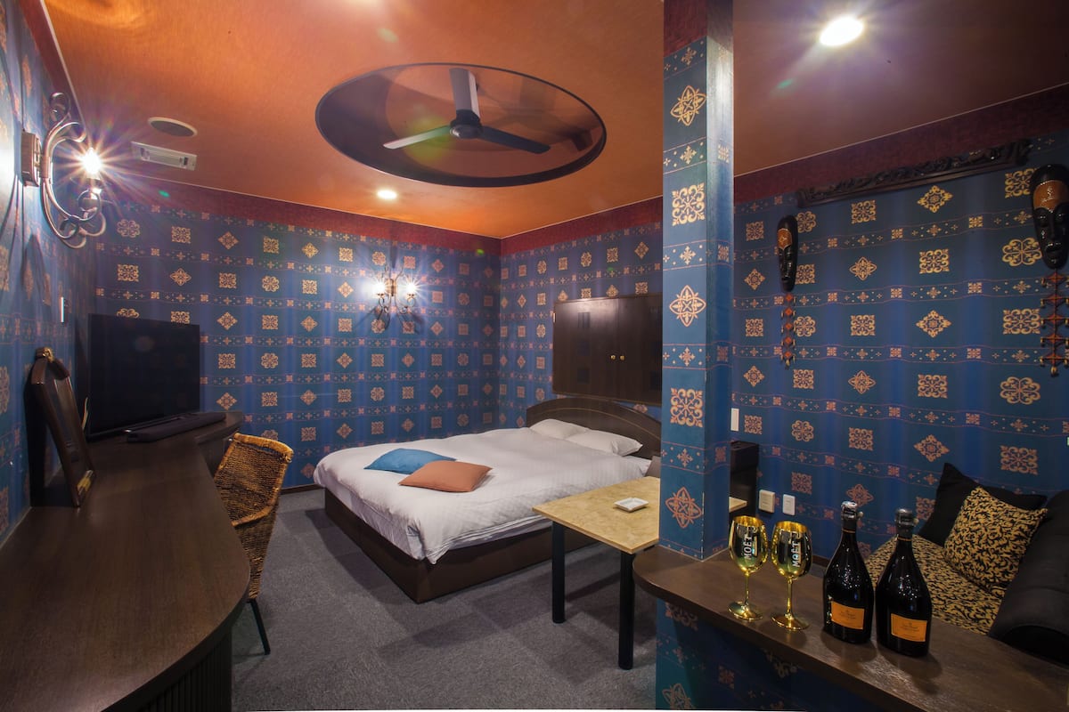 A room with a bed, a desk, and two bottles of wine on a counter.
