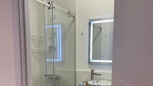 Une salle de bain moderne avec une douche à parois de verre, un meuble-lavabo en bois surmonté d’un vasque en marbre et des serviettes soigneusement pliées.