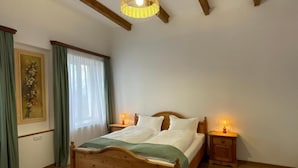 Une chambre à coucher avec un lit en bois, deux tables de chevet avec des lampes, une fenêtre avec des rideaux et un luminaire suspendu.