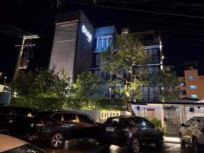 Um edifício com um letreiro grande com a letra 'DUM', cercado por carros estacionados e árvores.