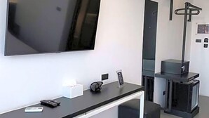 A modern hotel room with a flat-screen TV mounted on the wall, a small desk with a remote control, a digital clock, and a fireplace. - DUM Hotel (Chiang Mai)