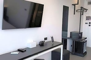 A modern hotel room with a flat-screen TV mounted on the wall, a small desk with a remote control, a digital clock, and a fireplace. - DUM Hotel (Chiang Mai)