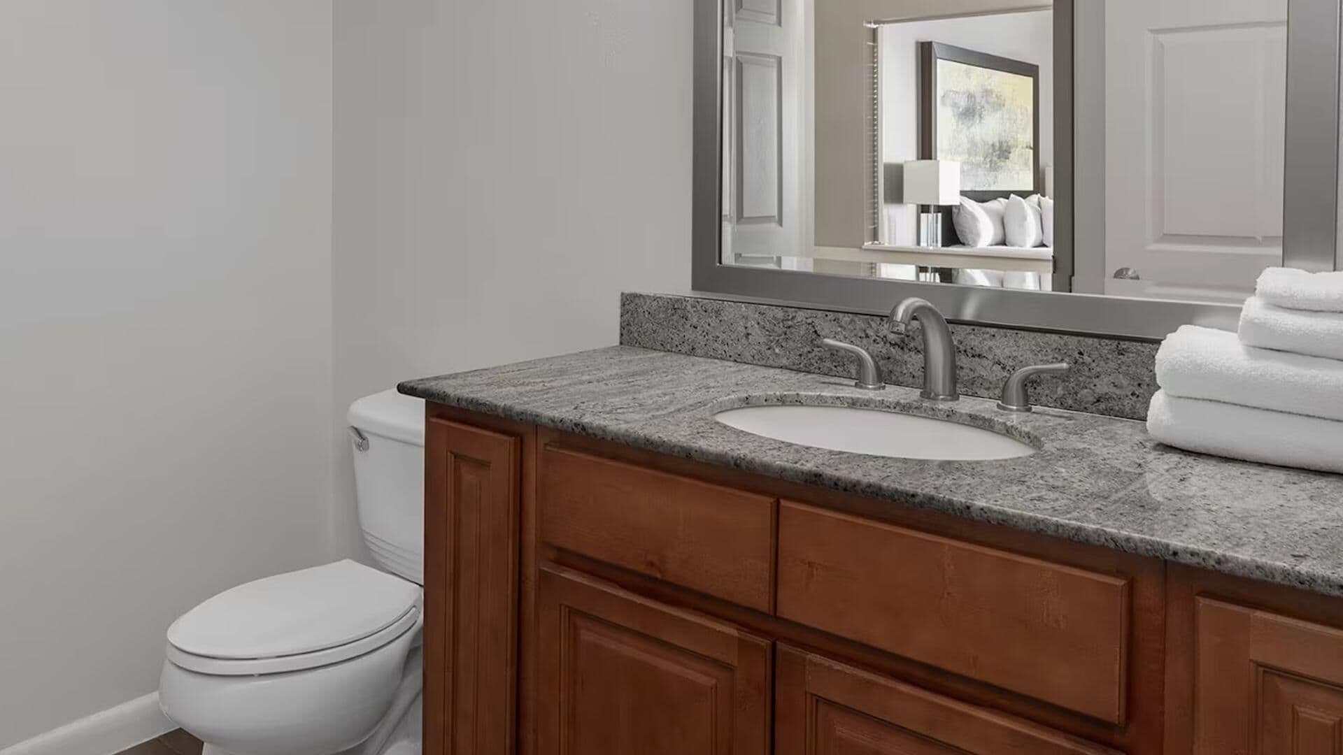 A bathroom with a white toilet, a granite countertop sink, and wooden cabinets.