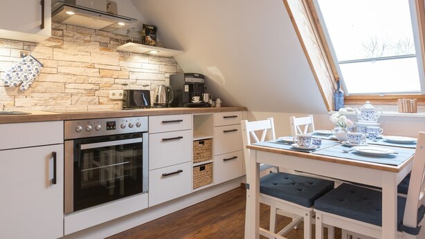 A kitchen with a stone backsplash, a coffee maker, and a dining area with a table set for two. - Apartment 'Ferienwohnung Lillebror' with Shared Terrace, Shared Garden and Wi-Fi (Olderup)