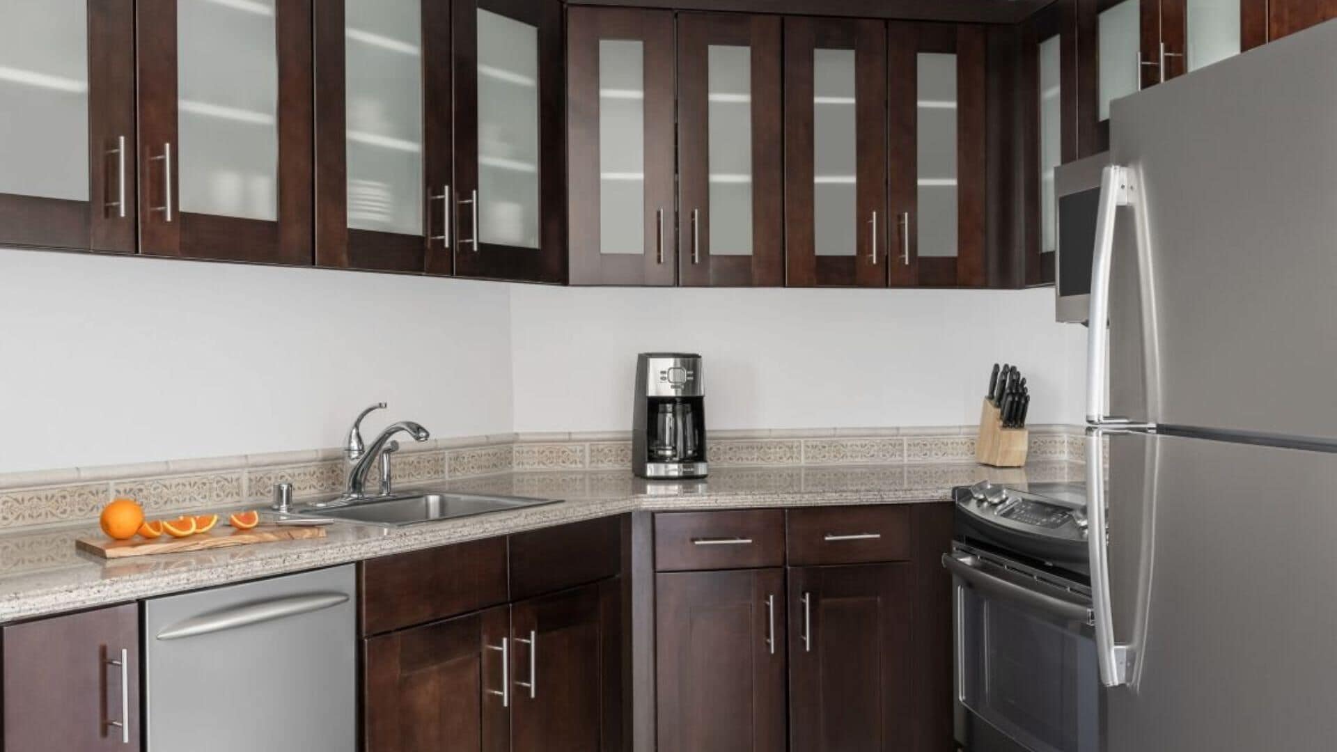 A modern kitchen with dark wooden cabinets, a stainless steel refrigerator, a coffee maker, and a sink.