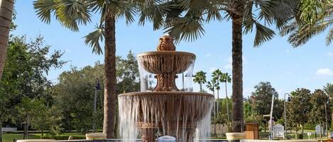 A multi-tiered fountain with water cascading down, surrounded by palm trees and a clear sky.