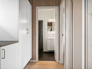 Ein schmaler Flur mit weißen Schränken und Holzboden, der zu einem Badezimmer mit Spiegel und Waschbecken führt.